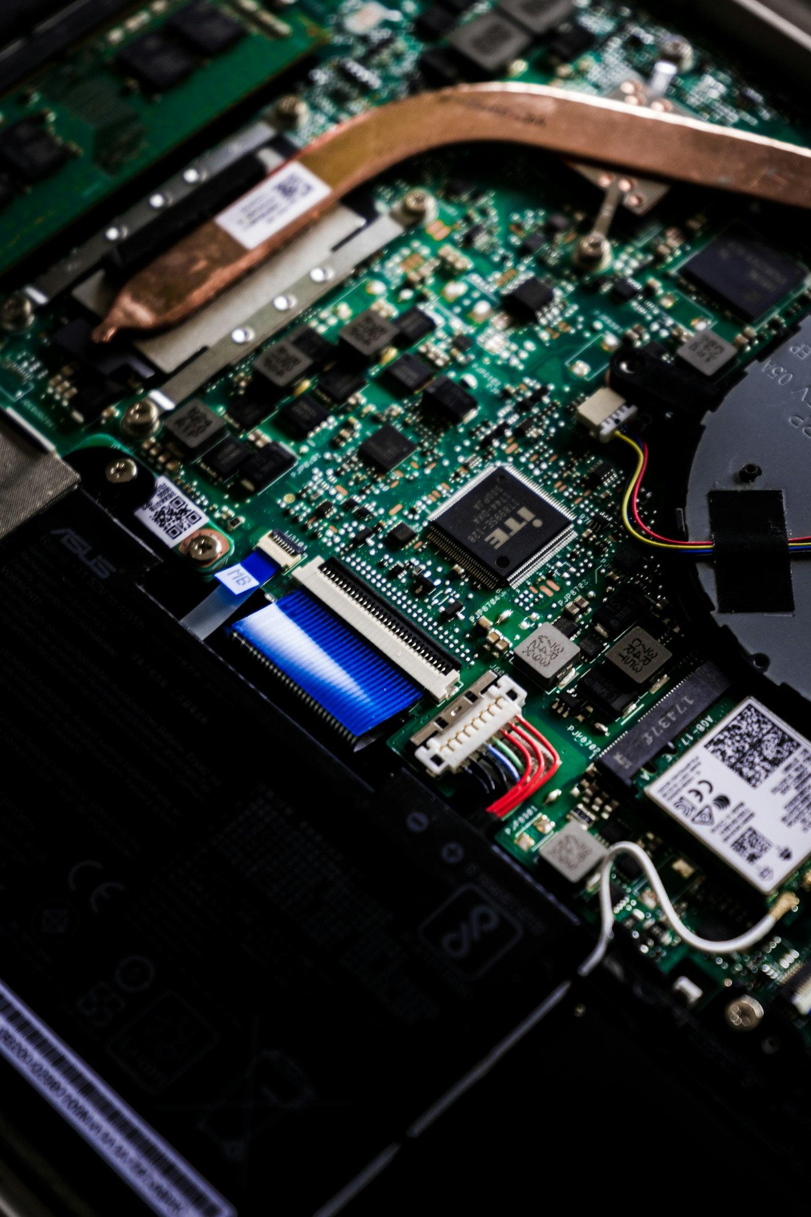 Premium notebook motherboard exposed on the bench during a Perth board-level repair — heat pipe, GPU and ribbon cables visible